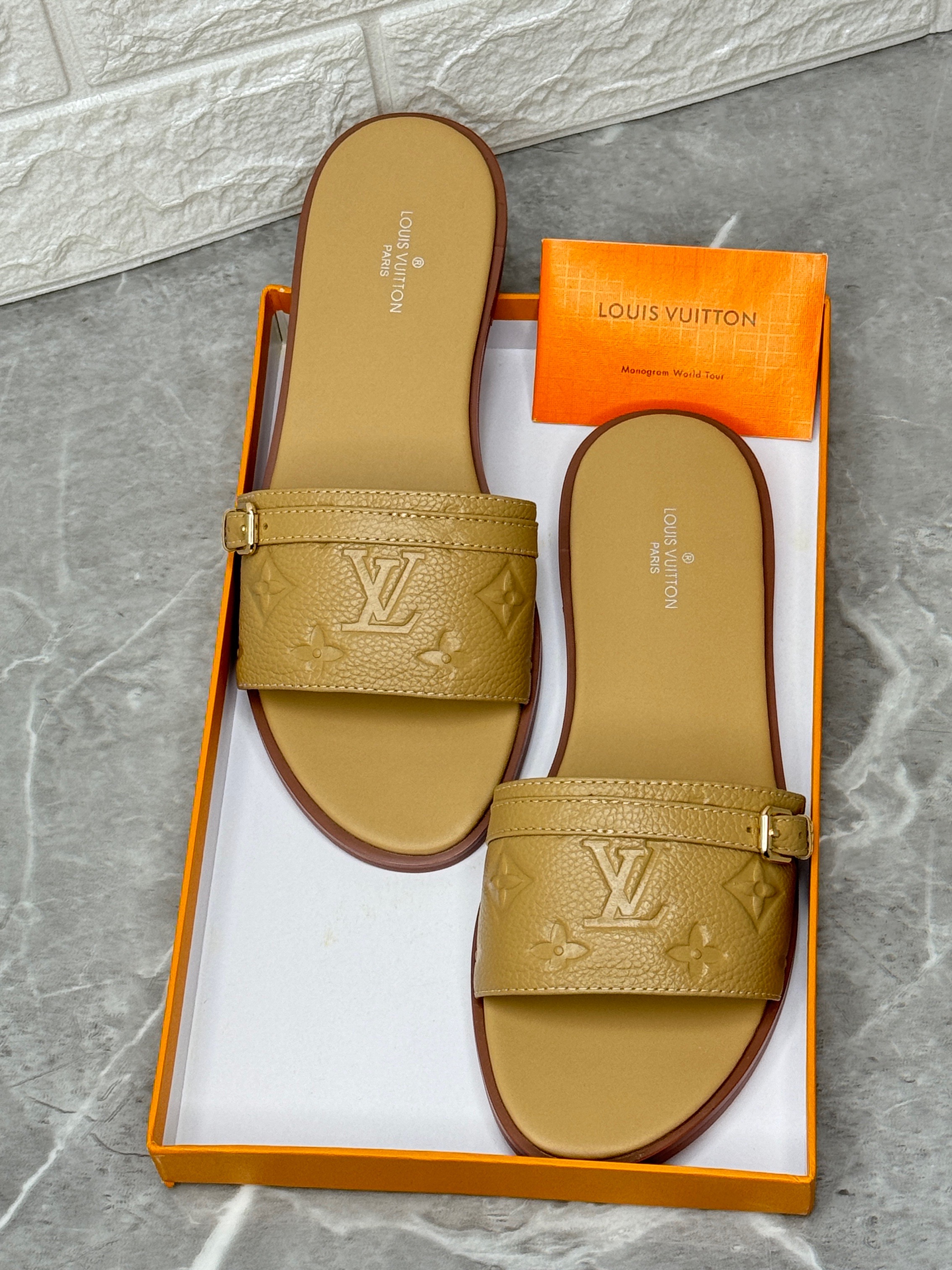 Louis Vuitton flat mules or slippers in a tan or brown color, featuring an embossed Monogram pattern and an adjustable strap with an LV accessory. image 1