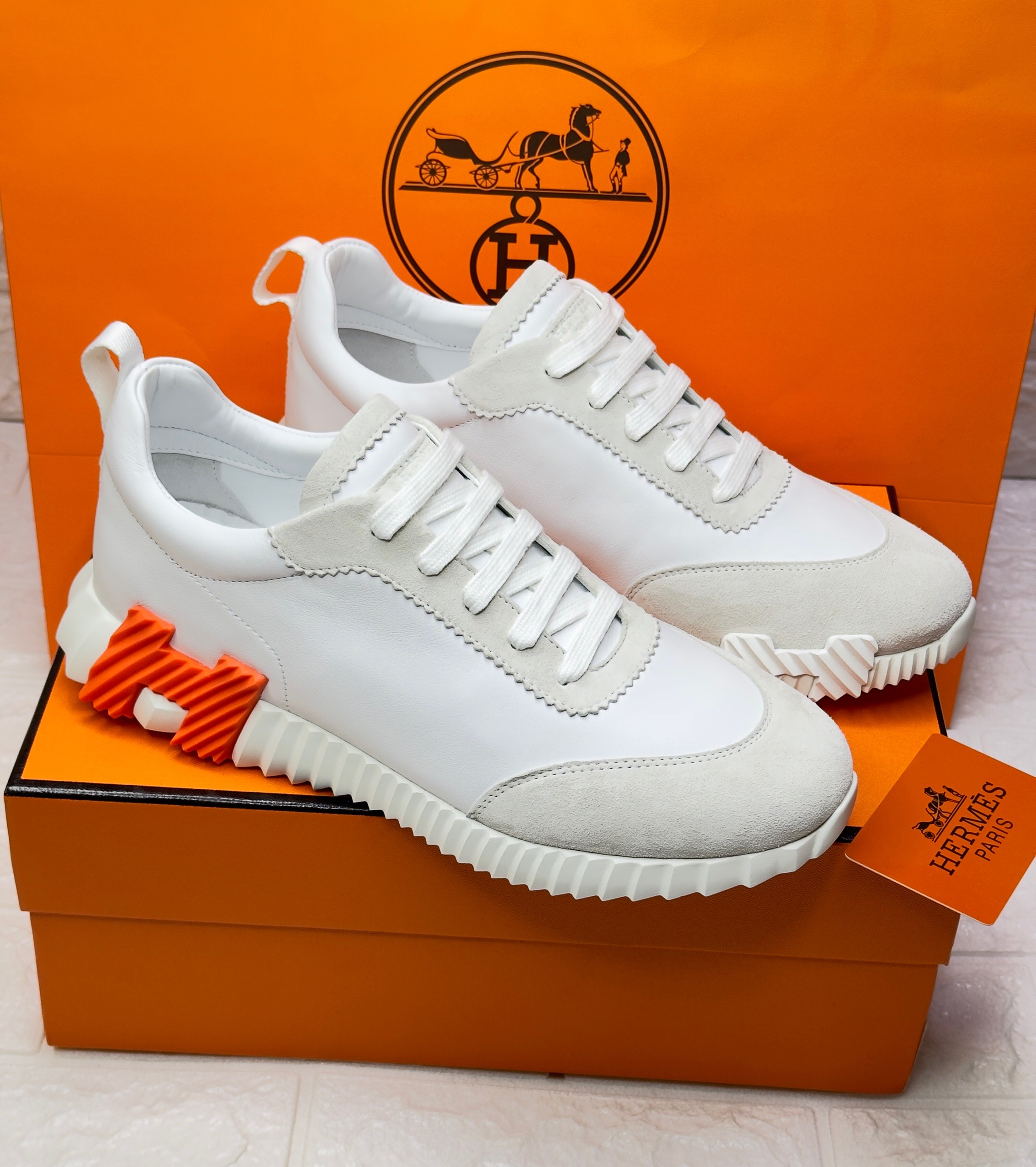 Herm?s Bouncing sneaker made of sport goatskin and suede, featuring a signature orange "H" motif on the heel and a cushioned rubber sole. image 1