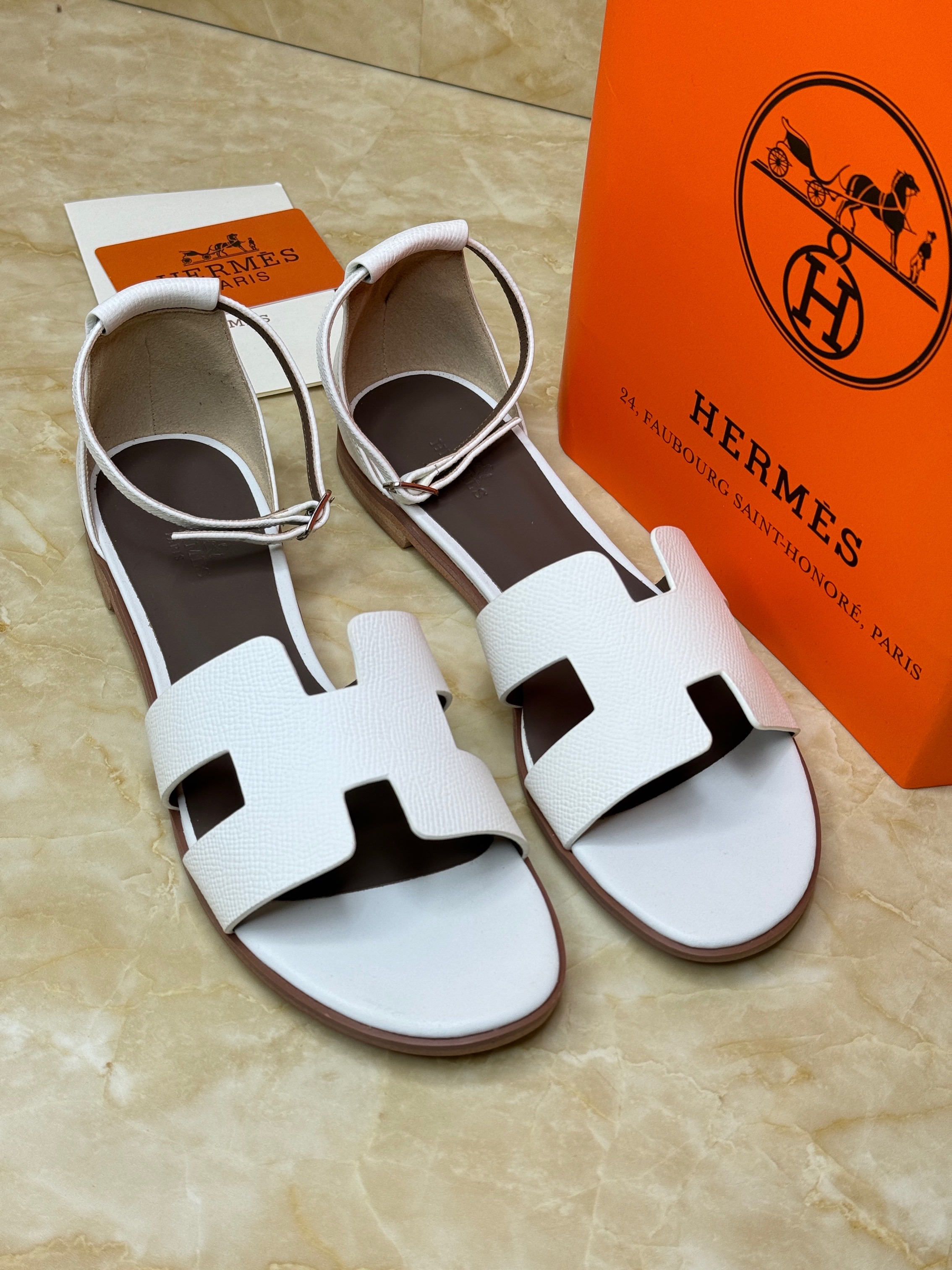 Herm?s Santorini sandals in a light color, possibly white or pale gray, featuring the iconic "H" cut-out detail and an adjustable ankle strap. image 1