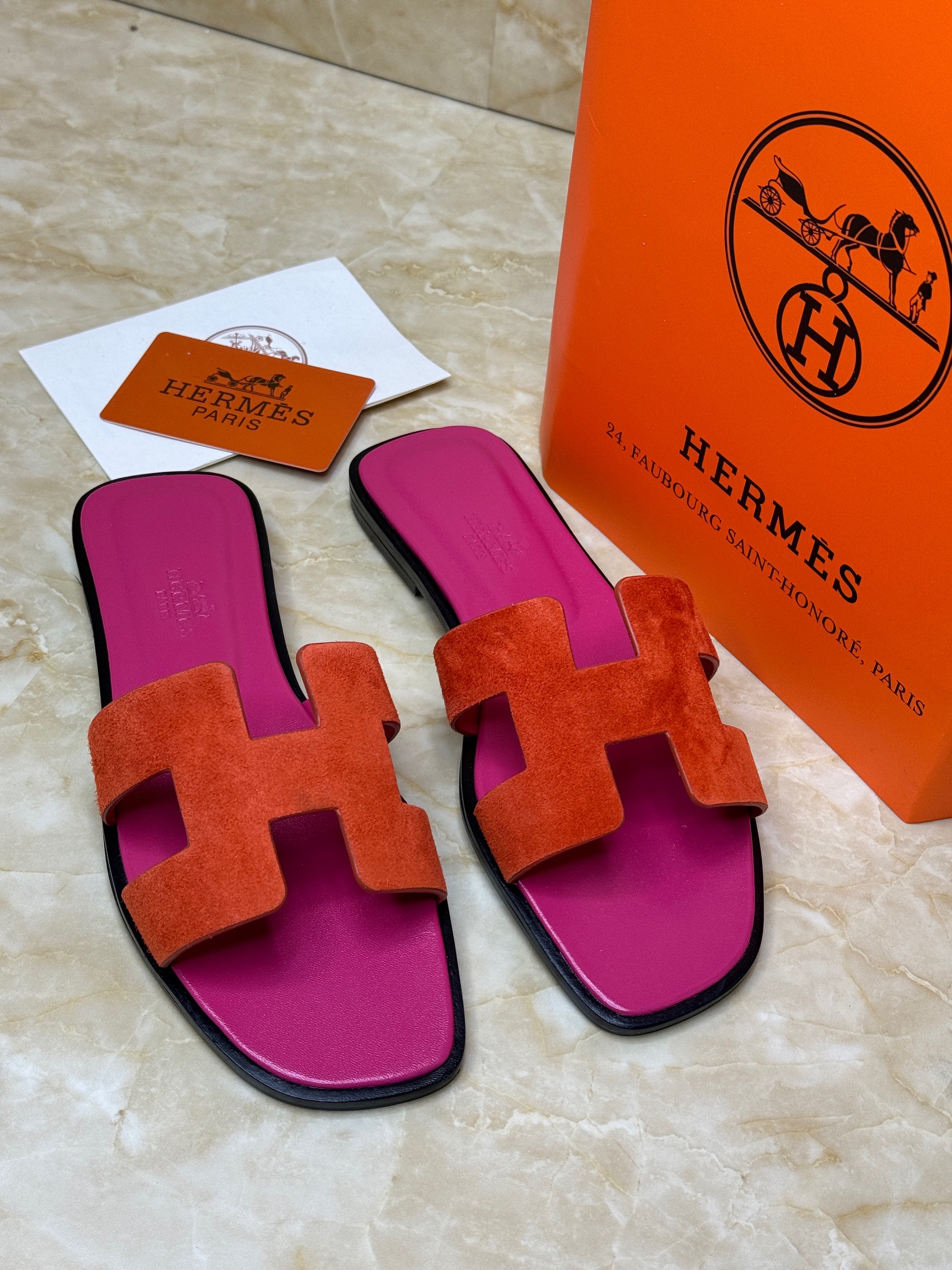 Herm?s Oran sandals, featuring the brand's iconic "H" cut-out on the upper strap. They are crafted from leather, with a vibrant orange suede H-strap and pink insoles. image 1